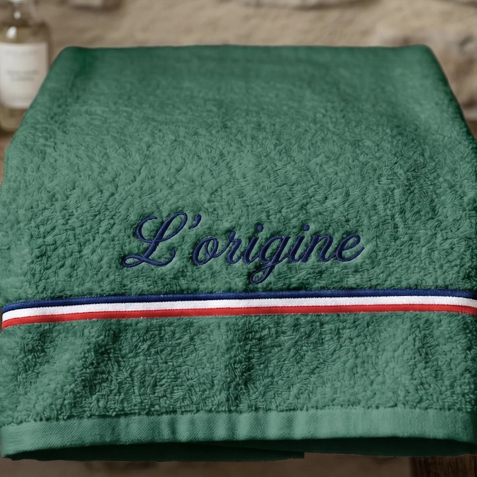 Serviette de bain verte en coton éponge avec une broderie bleu marine cursive 'L’origine' et une bande décorative tricolore (bleu, blanc, rouge)